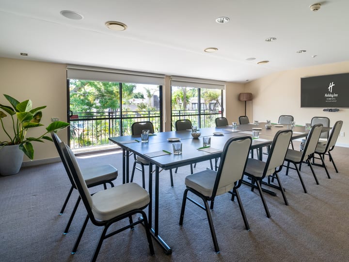Small meeting room with a U-shaped table layout, wall-mounted screen, and garden-view windows