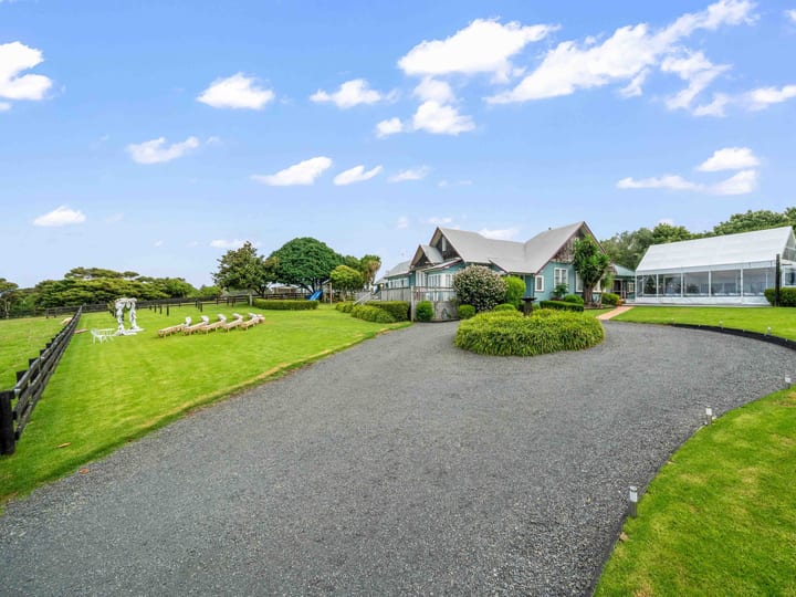 Gravel driveway curving to a dark-trimmed country house with steeply pitched roof, large lawn, white marquee to one side