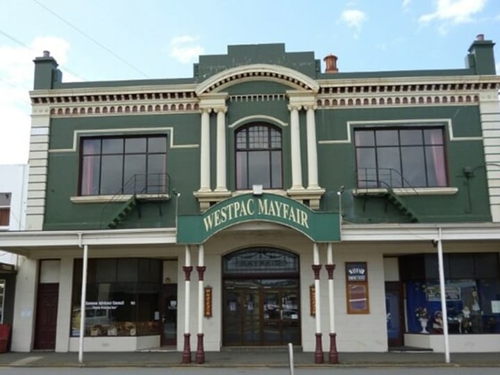 Two-storey green heritage commercial facade with white columns, arched windows, and ornate cornice