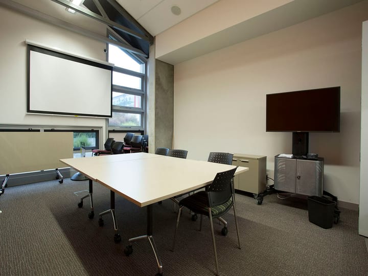 Small meeting room with table, chairs, projection screen and wall-mounted TV