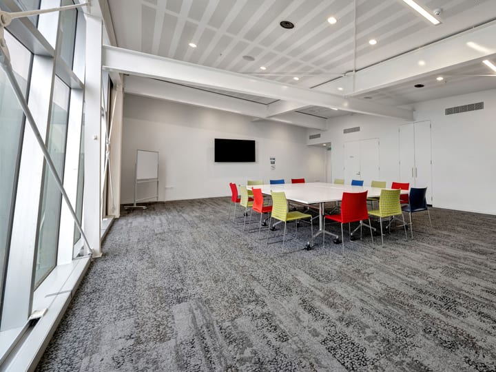 Meeting room with cluster of tables, coloured chairs and wall-mounted screen