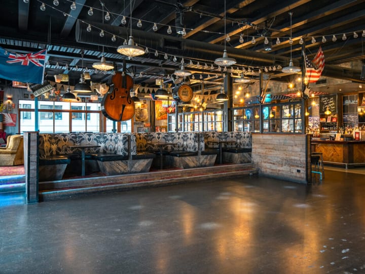 Eclectic bar interior with exposed trusses, patterned booths, large cello hanging from ceiling and music memorabilia