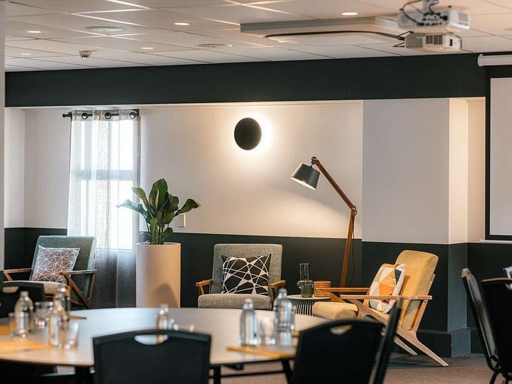 Modern breakout lounge with dark two-tone walls, mid-century chairs, floor lamp, and projector screen