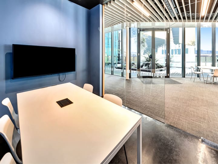 Small glass-enclosed meeting room with wall-mounted screen and harbour view