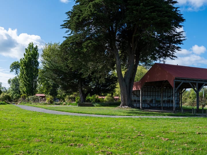Open-sided picnic shelter with red roof beside trees in a park