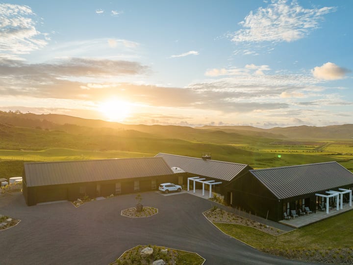Aerial view of dark-clad barn-style buildings set on rolling green hills at sunset