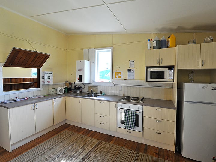 Plain kitchen with cream cabinetry, bench-top oven, microwave, and refrigerator, timber floor