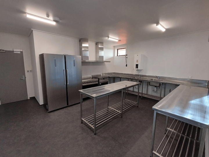 Stainless steel commercial kitchen with preparation benches, large fridge, range, and extraction hood