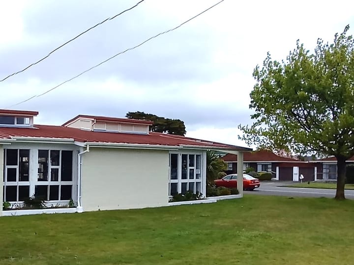 White rendered hall with stepped parapet and red-tiled roof wing, grassed surrounds