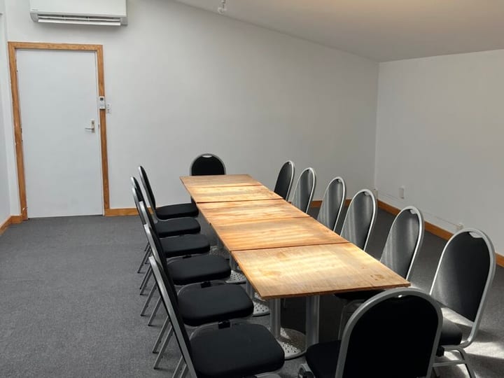 Plain white room with a long timber boardroom table and mixed black and grey chairs