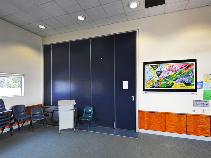 Meeting room with blue operable wall partition, stacked chairs and wall-mounted display