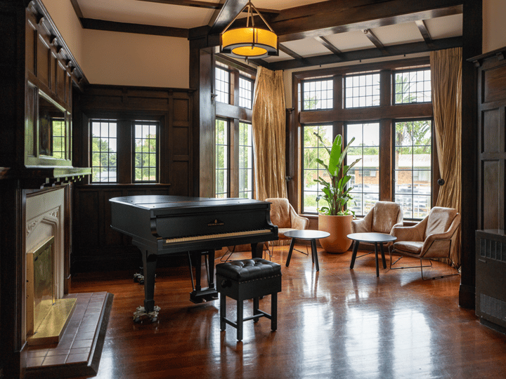 Room with dark timber panelling, grand piano, fireplace and leaded windows