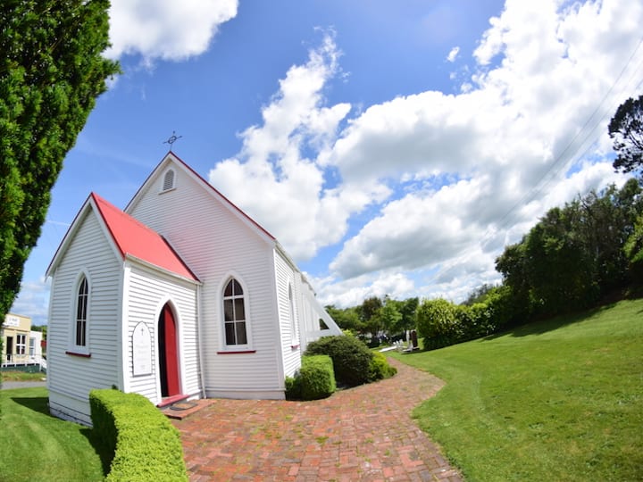 Small white-painted timber church with red-trimmed gable and red door, brick path entrance