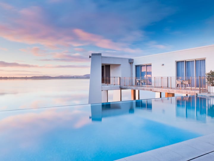 White render building with infinity pool at dusk, reflecting pink and blue sky over water