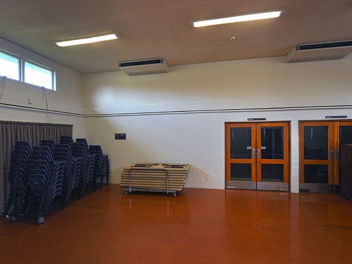 Empty hall with stacked chairs, folded tables and double timber doors