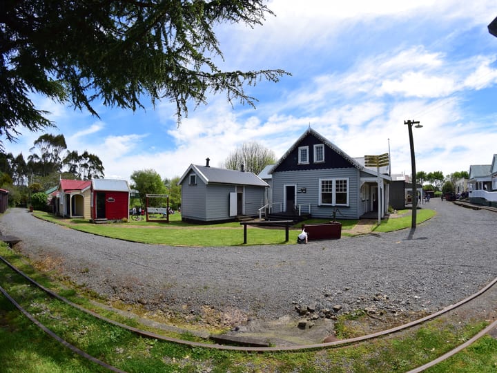 Open-air heritage village with weatherboard cottages, curved rail track, and gravel paths
