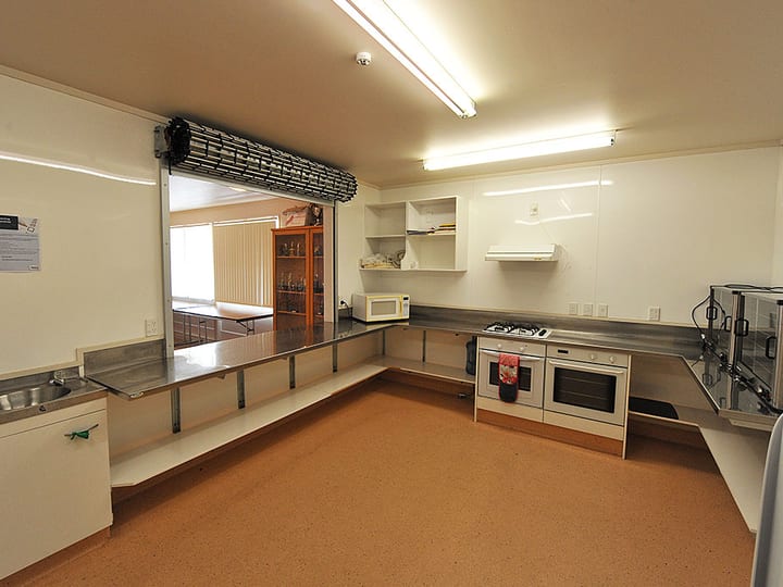 Catering kitchen with stainless benches, oven, fridge and serving hatch