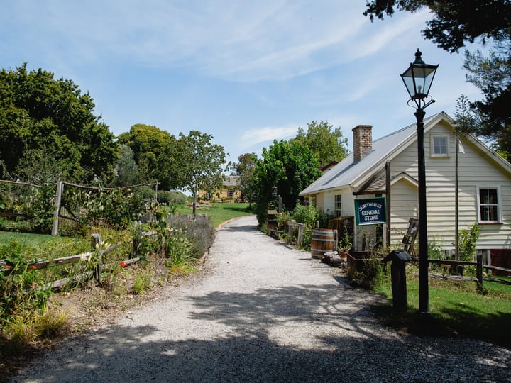 Gravel path through historical village with general store sign and period buildings