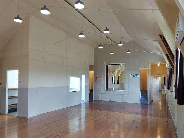Bare white hall interior with polished timber floor, high pitched ceiling, pendant lights, and serving hatch