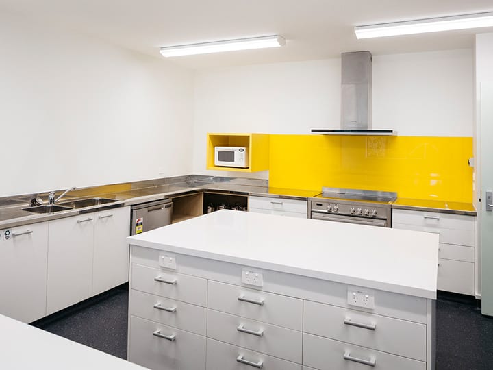 Catering kitchen with central island, yellow splashback, and stainless appliances