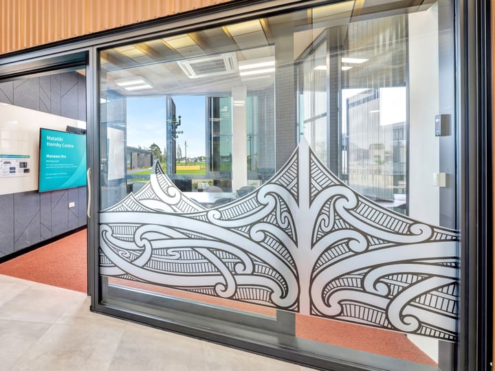 Glass entrance doors with decorative Māori-patterned etching on copper-clad building