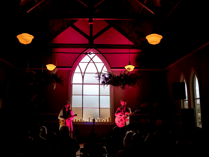 Gothic arched church interior lit in deep red with two musicians performing at the altar end