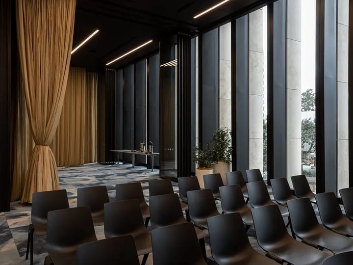 Dark-toned meeting room with floor-to-ceiling windows, city views, rows of dark chairs and gold drape partition