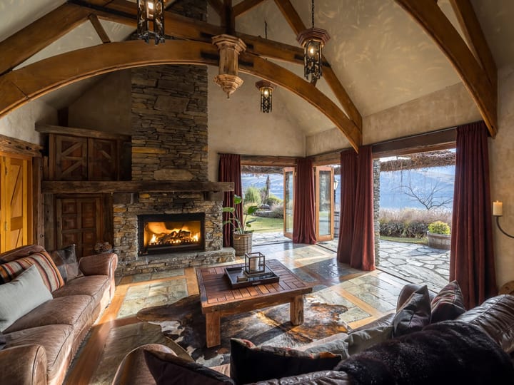 Stone fireplace lounge with vaulted timber beams, leather sofas, and open doors to garden view