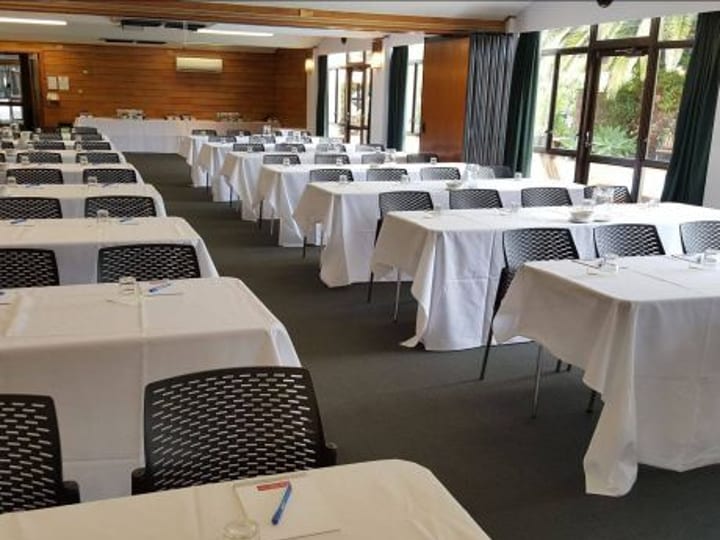 Timber-panelled function room with white tablecloths, dark chairs, large windows, and trees visible outside