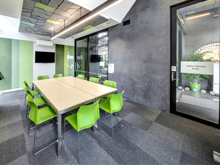 Meeting room with green chairs around a square table, concrete walls, and display screen