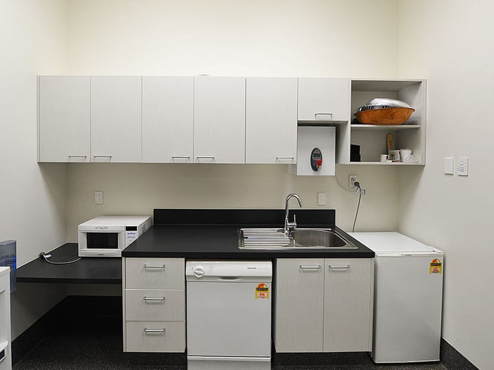 Small kitchenette with white cabinetry, sink, microwave and fridge