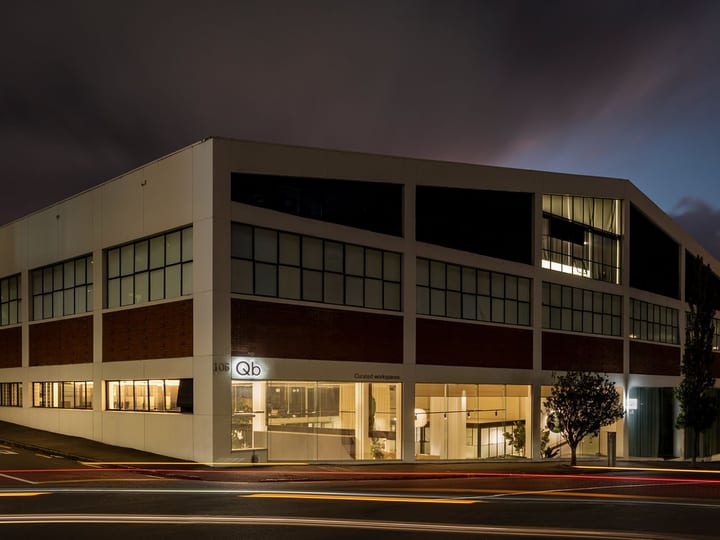 Three-storey brick and white commercial building with large glazed ground floor, night exterior