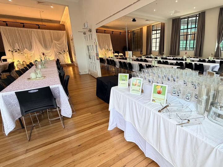 Hall interior with timber floor, round tables dressed in white linen, draped backdrop, and tall windows