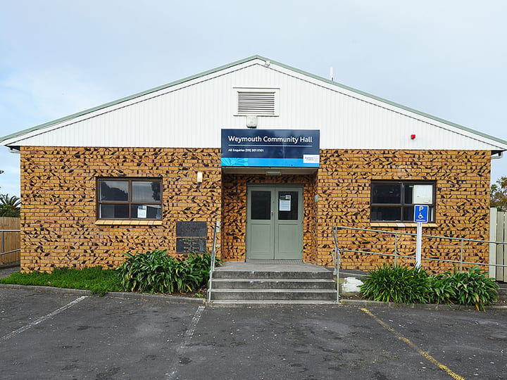 Tan brick hall with gabled white fascia, double green doors, and car park entry