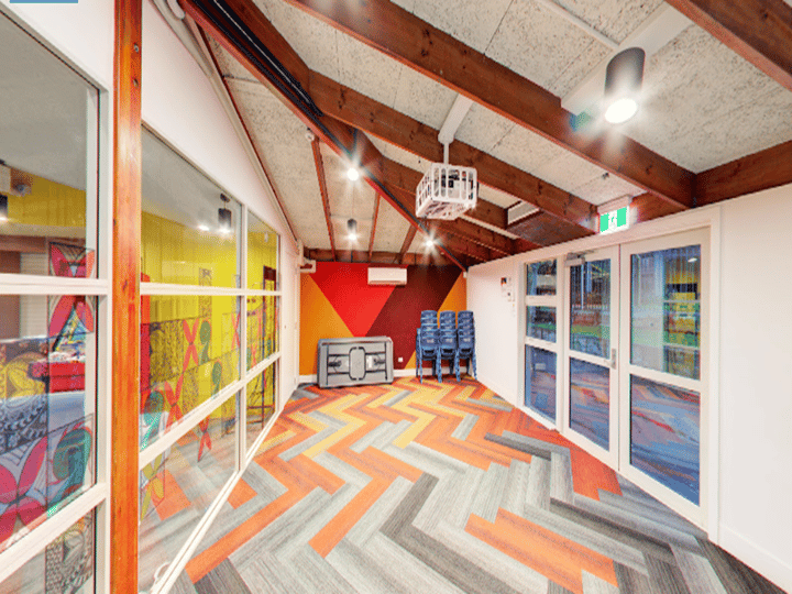 Open hall with exposed timber rafters, herringbone carpet, colourful geometric wall mural