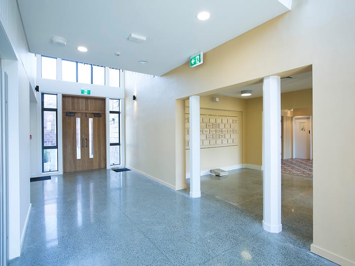 Foyer with polished concrete floor, timber doors and columned archway into a hall