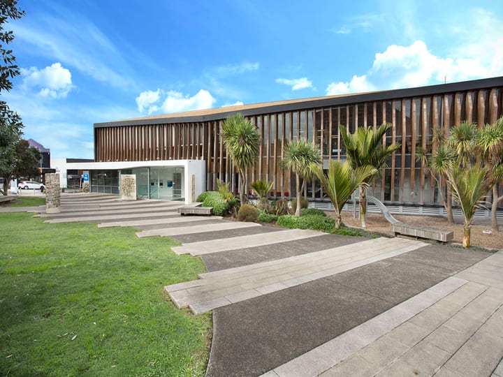 Low-rise contemporary building with horizontal timber louvre cladding, glass entry, and paved approach with planted borders