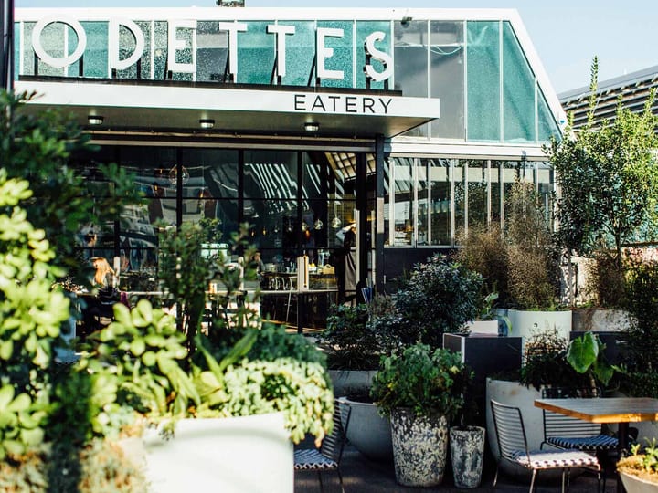 Rooftop eatery exterior with glass greenhouse addition, lush planted terrace and seating, black steel frame