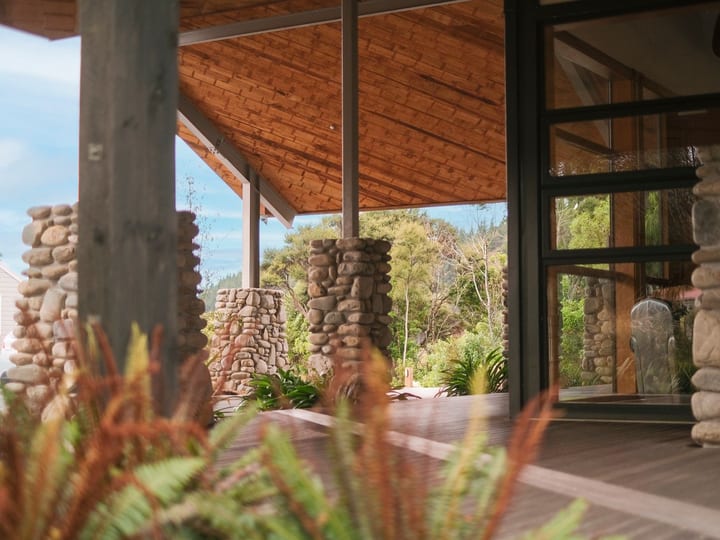 Stone and timber covered entry with stacked-stone columns, timber ceiling, and native planting
