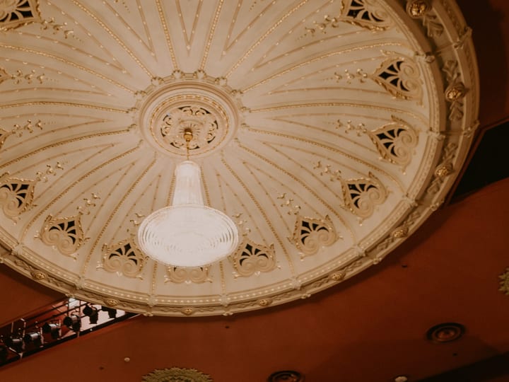 Ornate cream domed ceiling with gold detailing and a central pendant light fixture, terracotta walls