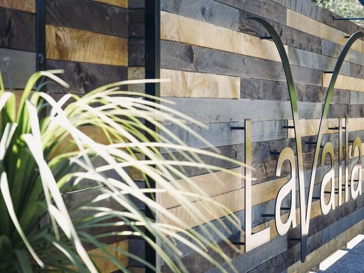 Horizontal timber-clad fence with a metal venue sign, green foliage in the foreground