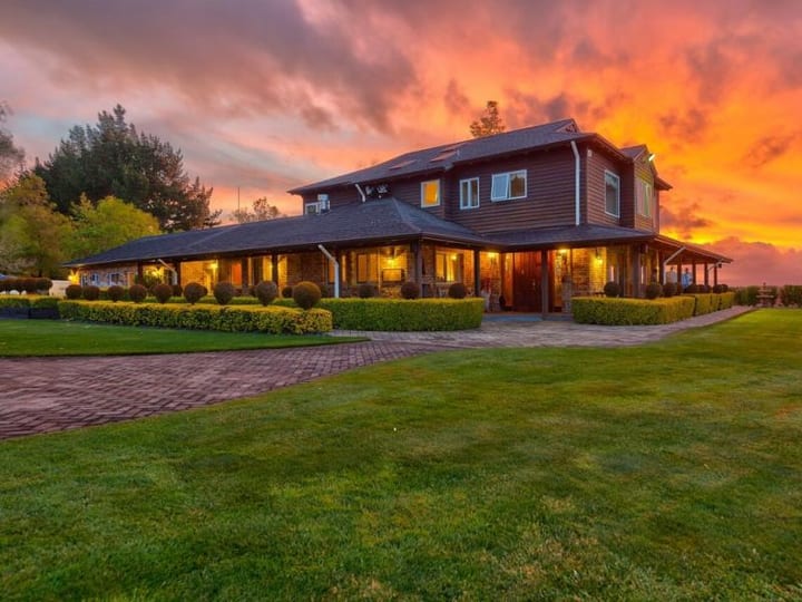 Timber homestead exterior at sunset with manicured lawn and topiary hedges
