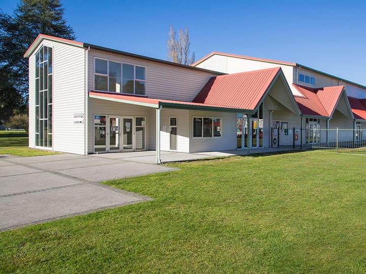 Long low building with white weatherboard cladding and red metal roof, set on a large lawn