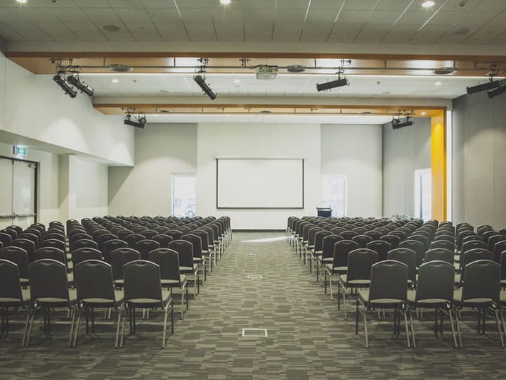 Large conference hall with rows of chairs and projection screen at front