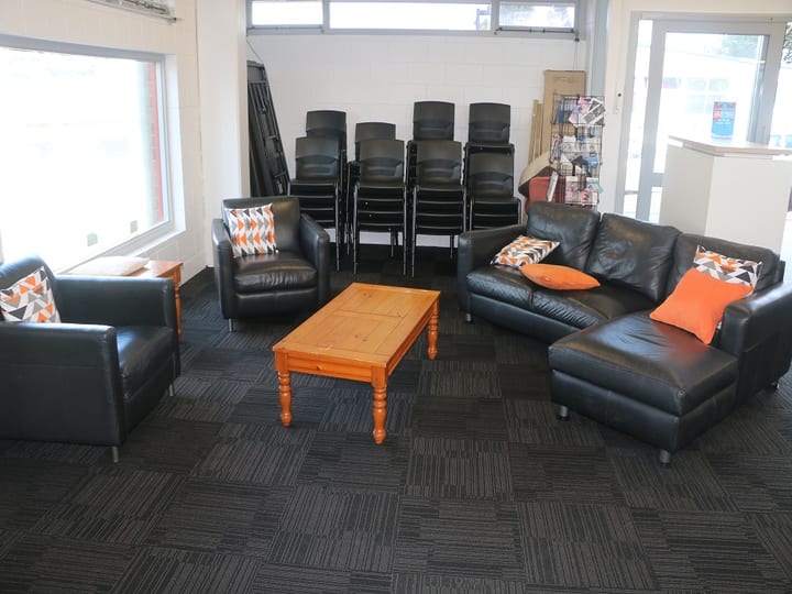 Lounge area with black leather sofas, orange cushions, coffee table, and stacked chairs in background