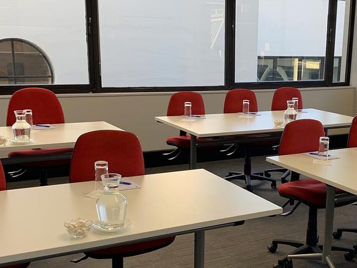 Meeting room with table set for small group, red chairs, harbour view