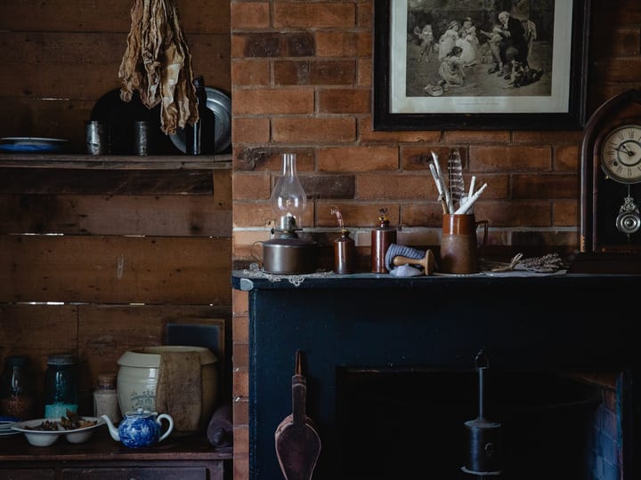 Period kitchen interior with dark wood shelving, antique crockery, stove and brick fireplace
