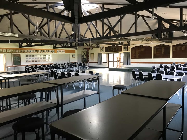 Large club hall with exposed dark timber roof trusses, tables, and club memorabilia on walls