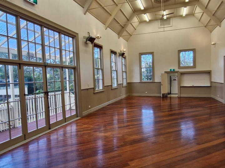 Timber-floored hall with high vaulted ceiling, exposed rafters, tall windows and verandah doors