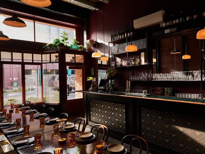 Deep red-walled dining room with patterned tile bar front, amber pendant lights and long table setting